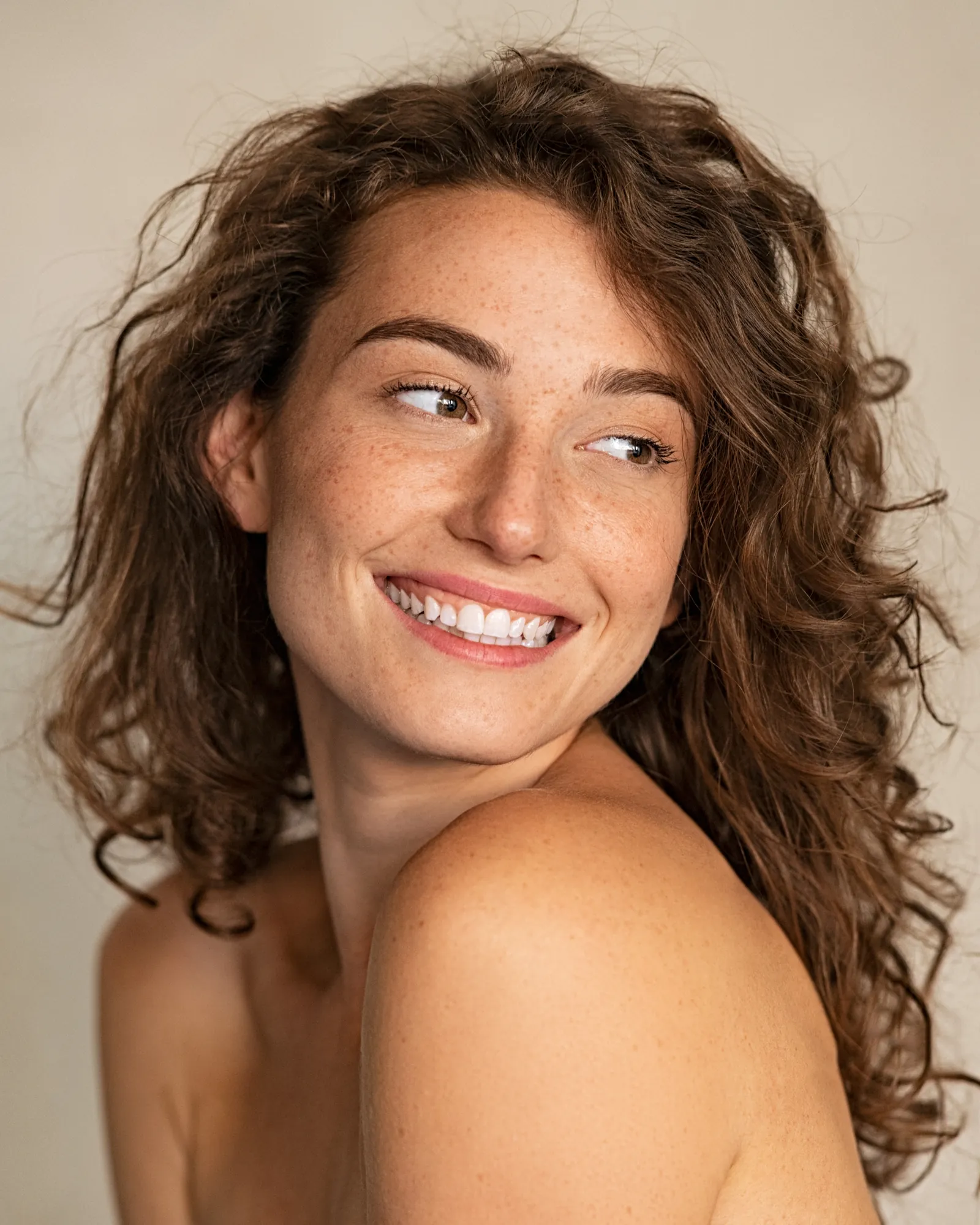 A smiling woman with curly hair glancing over her shoulder