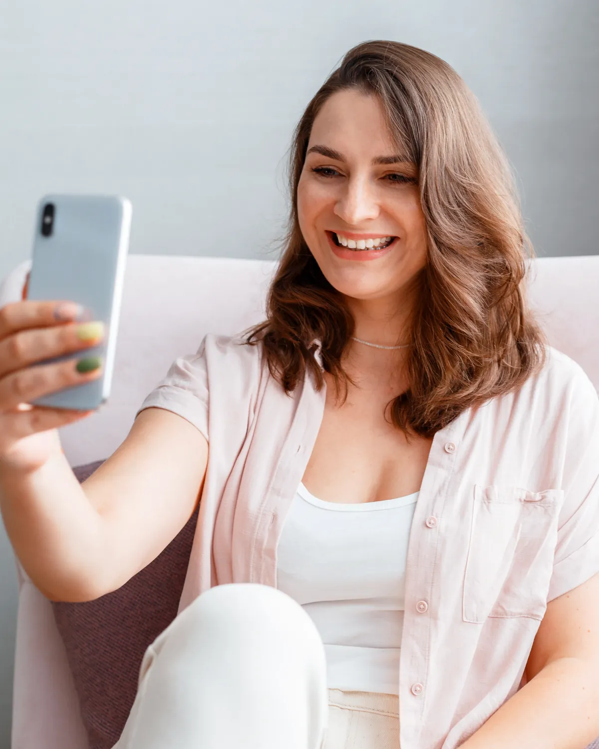 A smiling woman taking a selfie on her phone at home